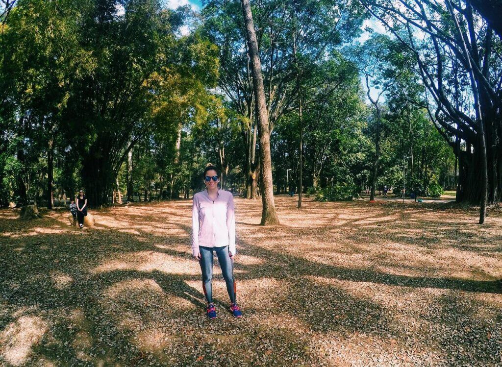 Manuela Brasão veste casaco esportivo rosa, legging cinza e tênis de corrida azul no Parque Ibirapuera em São Paulo.