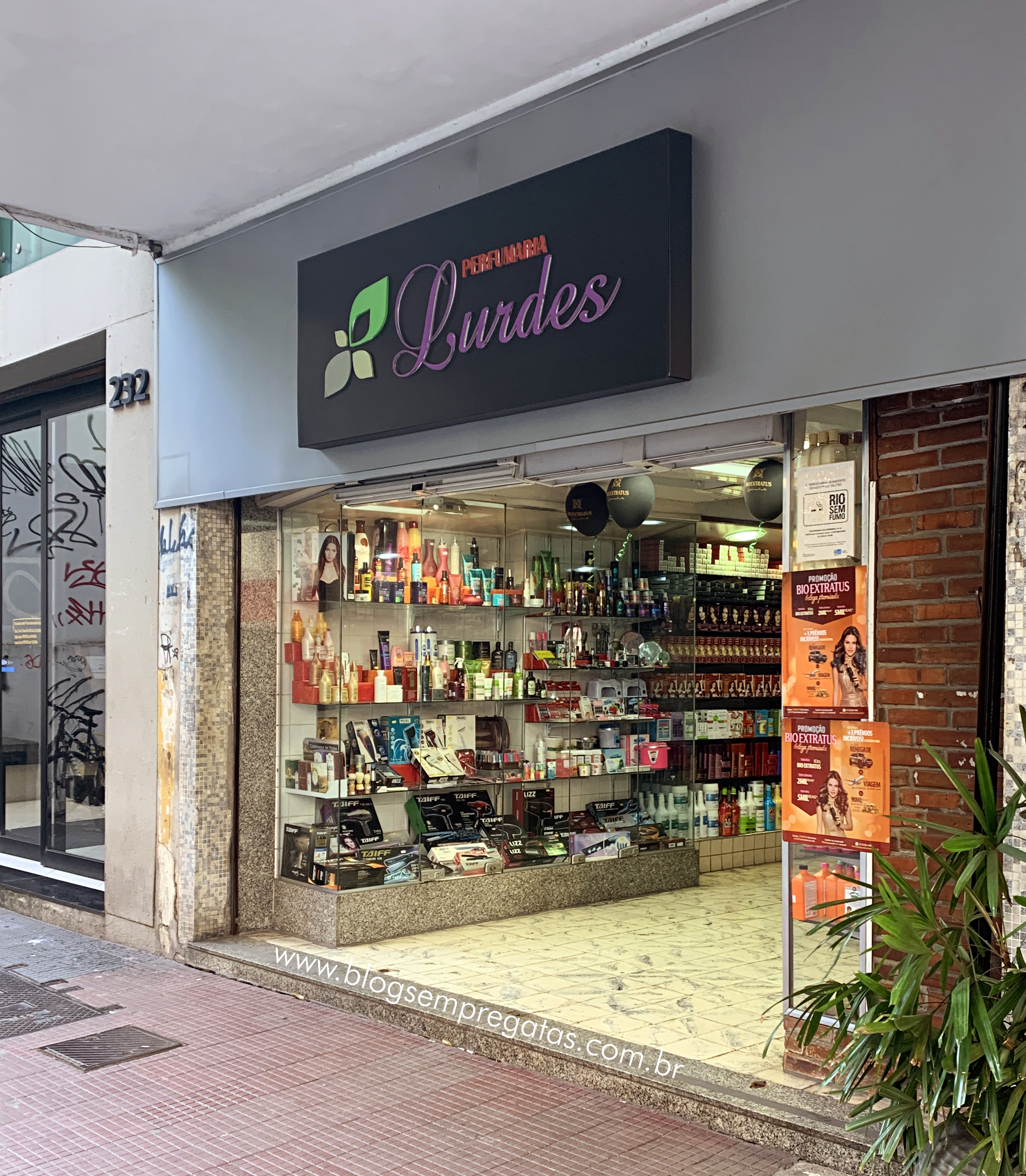 Entrada da Perfumaria Lurdes com letreiro com nome da marca e vitrine de produtos.